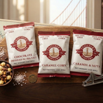 Three packages of Thatcher's Popcorn on a wooden board with a decorative background
