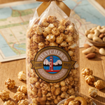 Gourmet popcorn bag with a bow, surrounded by scattered popcorn and cashews on a wooden surface.