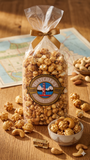 Gourmet popcorn bag with a bow, surrounded by scattered popcorn and cashews on a wooden surface.