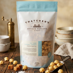 Bag of Thatcher's Artisan Popcorn on a wooden table with popcorn and caramel candies.