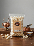 Bag of Taster's Choice kettle popcorn on a wooden table with a copper kettle and small bowl.