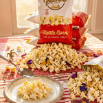 Popcorn on a plate and scattered on a table with Thachers Kettle Corn bags in the background.