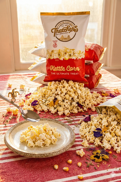 Popcorn on a plate and scattered on a table with Thachers Kettle Corn bags in the background.