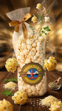 Bag of popcorn with a decorative label on a wooden surface, surrounded by popcorn kernels and herbs.