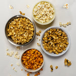 Four bowls of popcorn in different flavors on a light gray background