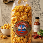Bag of Hatcher's popcorn with sriracha sauce on a wooden surface with a map in the background