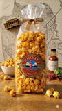 Bag of Hatcher's popcorn with sriracha sauce on a wooden surface with a map in the background