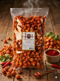 Bag of Thatcher's Sriracha popcorn on a wooden surface with additional popcorn and red peppers.