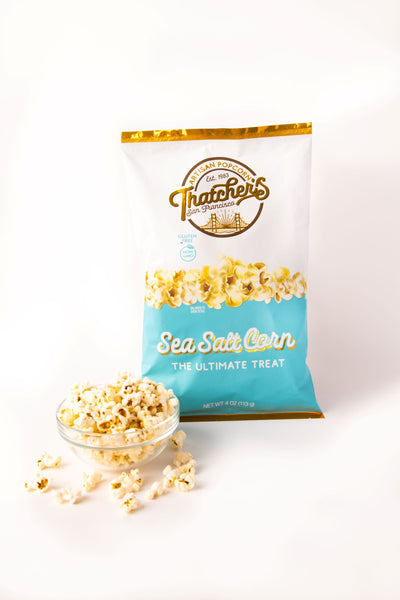 Bag of Thatchers Sea Salt Corn popcorn on a wooden table with popcorn and salt.
